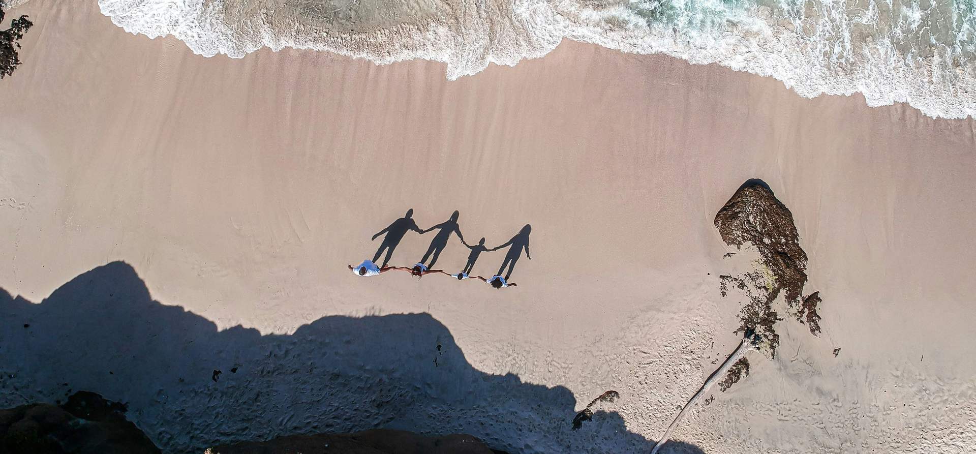 A family holding hands on the beach, seen from above