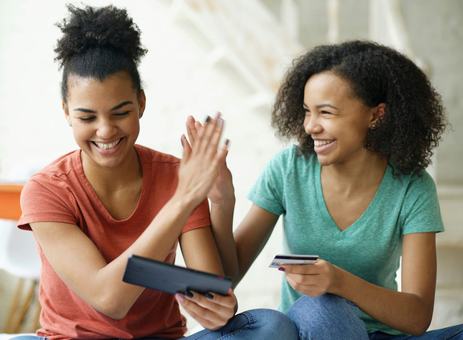 Two smiling friends giving each other a high five, one holding a bank card